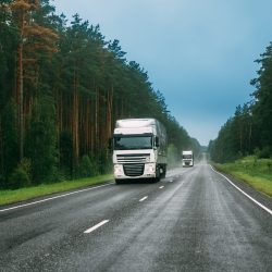 White Truck Or Tractor Unit, Prime Mover, Traction Unit In Motion On Road, Freeway. Asphalt Motorway Highway Against Background Of Forest Landscape. Business Transportation And Trucking Industry
